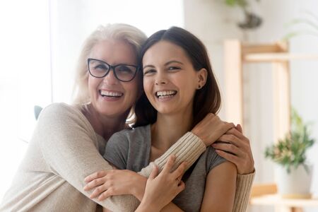 Portrait of happy senior 60s mom and grown-up daughter hug cuddle enjoy weekend time together, smiling mature mother and adult millennial girl child embrace show love and care in relationshipsの写真素材