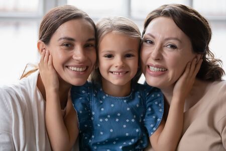 Portrait of little preschooler girl hug smiling young mother and senior grandmother, happy three...
