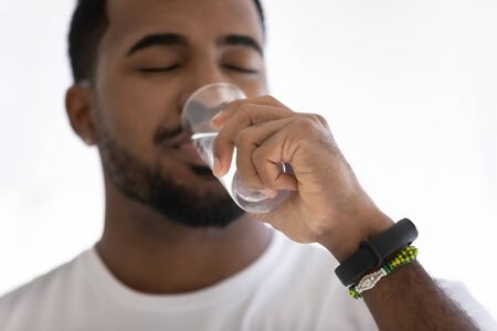 Close up of young african American man feel thirsty drink enjoy clean mineral still water from...