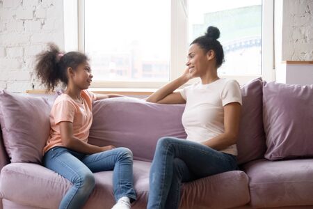African family spend time at home mother sitting on couch with pre-teen daughter women talking...