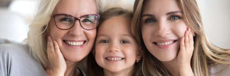 Little girl her young mother and mature grandma portrait. Multi generational women faces smiling looking at camera close up view photo, family bond concept. Horizontal banner for website header designの写真素材