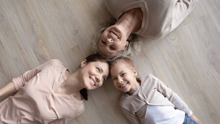 Top view portrait of smiling three generations of women lying on warm wooden floor at home having fun together, overjoyed girl with young mom and senior grandmother relax enjoy family weekendの写真素材
