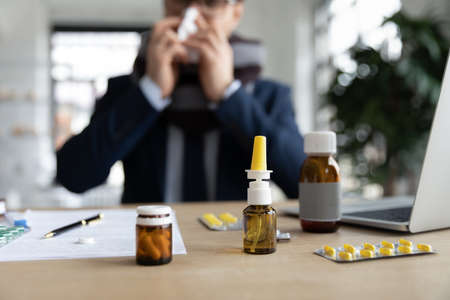 Close up of sick worker blow nose suffer from flu fever at workplace, take medication to relieve sickness symptoms, ill male employee have meds pills from influenza or cold, health problem conceptの写真素材