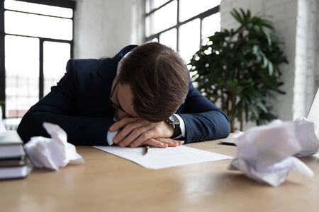 Tired male employee or worker feel fatigue exhaustion sleep or take nap at workplace, overwhelmed exhausted businessman fall asleep in office, preparing business report on deadline, overwork conceptの写真素材