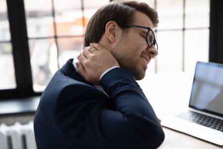 Unwell caucasian businessman touch neck struggle with muscular spasm or strain from incorrect posture, unhealthy male employee suffer with backache, have painful back feeling, sedentary life conceptの写真素材