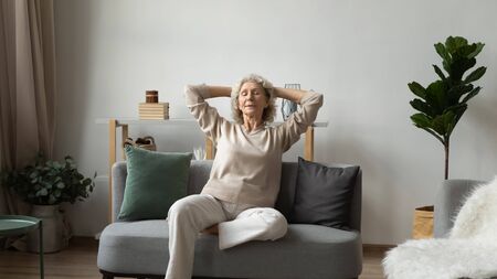 Happy calm elderly woman sit relax on sofa in living room breathing fresh air at home, peaceful mature 60s female rest on comfortable couch taking nap or meditating, stress free, peace conceptの写真素材