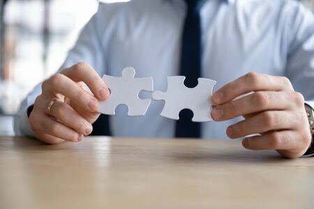 Crop close up of hands of Caucasian businessman hold assemble jigsaw find perfect business solution at workplace, male employee put together join puzzle, make decision or solve business problemの写真素材