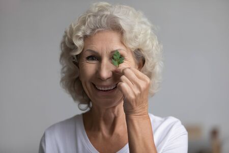 Headshot portrait of smiling mature woman hold fresh parsley recommend garnish for natural teeth whitening, happy elderly female use greenery organic cosmetics for skincare oral care daily routineの写真素材
