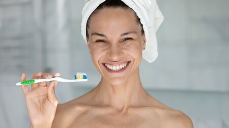 Head shot overjoyed beautiful woman wearing white bath towel on head holding toothbrush with...