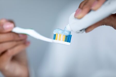 Close up African American woman applying toothpaste on toothbrush, holding in hands, girl squeezing dentifrice from plastic tube, personal oral hygiene and care, caries prevention, morning routineの写真素材