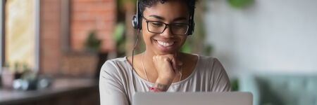 African girl wear headphones looks at pc screen watch movie, online webinar, enjoy virtual study...