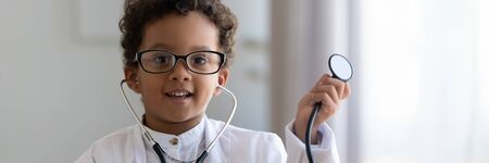 African boy wear glasses white coat uniform hold stethoscope play doctor pretend therapist worker, close up. Pediatry medical industry, childcare concept. Horizontal banner for website header designの写真素材