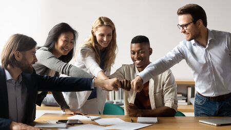 Horizontal image middle-aged and young five multiracial staff members gather in boardroom show unity stacked hands in circle, fists bumping symbol of togetherness common goals business loyalty conceptの写真素材