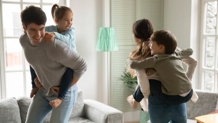 Small preschooler children piggyback young parents engaged in funny game at home together, overjoyed little kids have fun play with loving smiling mom and dad, enjoy family weekend activityの写真素材