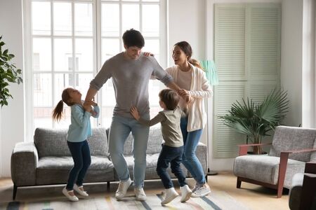 Overjoyed Caucasian young family with little kids have fun dancing and jumping together in living room, happy parents feel playful involved in funny game with small preschooler children at homeの写真素材