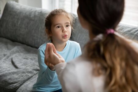 Small preschooler disabled girl practice nonverbal talk with female nanny or tutor at home, cute little child make hand gesture learn speak sign language with mother, children disability conceptの写真素材