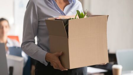 Horizontal photo businesswoman holding cardboard box with belongings and plant in hands, new hired or promoted employee intern first working day concept, standing in office, woman get jobの写真素材