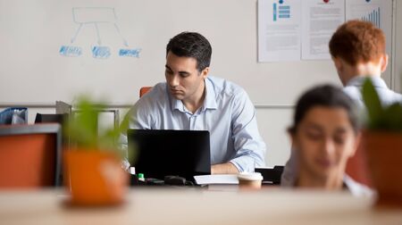 Serious busy businessman employee working on laptop in coworking space with colleagues, looking at computer screen, using software, writing report or analyzing project statistics, horizontal photoの写真素材