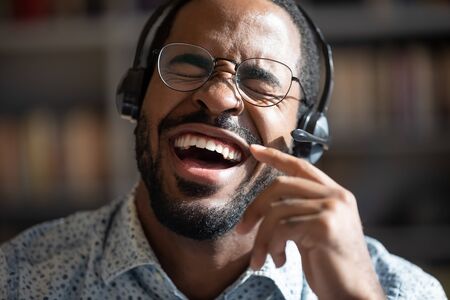 Close up portrait excited African guy wearing headset singing song alone indoors. Employee having fun during break, man enjoy favourite track, relish weekend and hobby, music lover modern tech conceptの写真素材