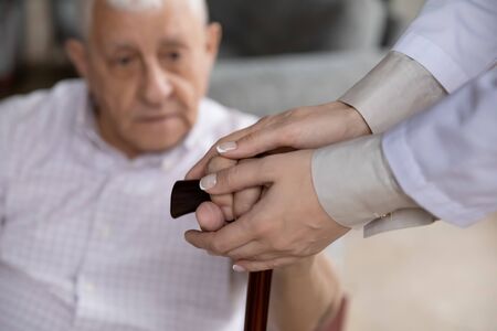 Close up female caregiver holding mature patient hands on cane, caring doctor therapist supporting comforting elderly disabled man, expressing care and empathy, healthcare and psychological helpの写真素材
