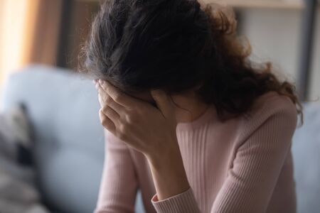 Close up frustrated depressed woman touching forehead, feeling headache, sitting on couch alone, lost in thoughts, unhappy sad girl suffering from break up or divorce, unexpected pregnancyの写真素材