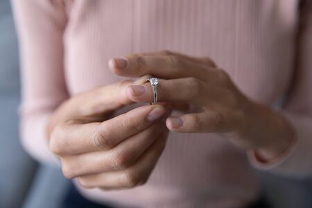 Close up young woman taking off wedding ring, divorce concept, female hands holding engagement ring,...