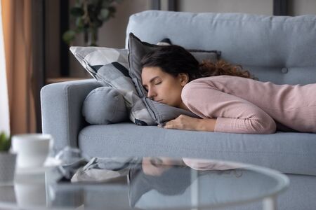 Tired peaceful beautiful woman sleeping on cozy couch in living room, lying on stomach, exhausted young female with closed eyes resting on sofa, taking nap, enjoying lazy weekend at homeの写真素材