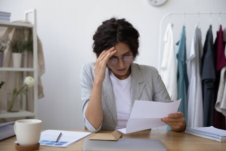 Upset young woman sit at desk feel frustrated with dismissal notice news in paperwork document,...