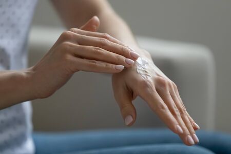 Close up view young woman sitting indoor applying moisturizing nourishing cream for hands. Organic...