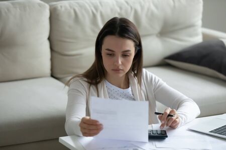 Disappointed housewife managing family budget read notification, received bad news bank inform client about penalty of debt. Focused woman calculating expenses, analyzing financial statement conceptの写真素材