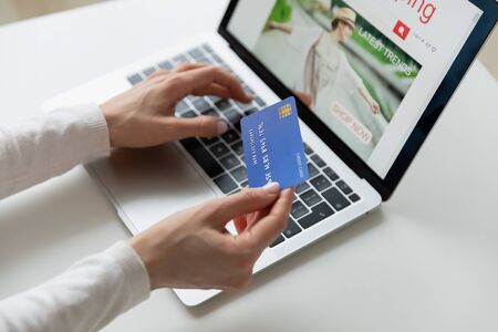 Close up of female hands holds credit card makes secure payment online using laptop buying in...