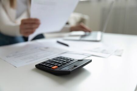 Close up view on coffee table lie calculator papers documents unrecognizable woman working on laptop indoor. Small business owner do analyze income and expenses, pay bills use internet banking conceptの写真素材