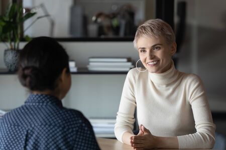 Two women sit in front of each other at desk in office communicating during formal meeting. HR manager and vacancy candidate talking at job interview, client and company manager negotiating conceptの写真素材