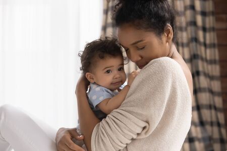 Close up loving African American young mother holding adorable toddler daughter, cuddling, family enjoying tender moment together, caring mum hugging cute little girl with closed eyes, childcareの写真素材
