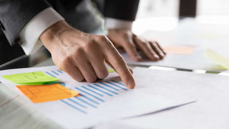 Crop close up of male employee point at graph reading consider paper company financial statistics at...