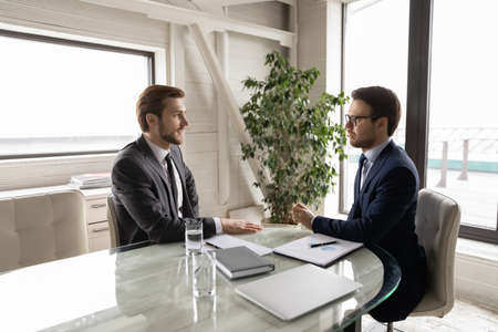 Concentrated Caucasian director talk with male client or customer at business meeting in boardroom, focused businessmen or partners speak discuss partnership at office briefing, collaboration conceptの写真素材