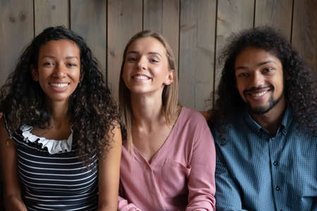 Group of happy multi racial friends mixed-race african and caucasian intimates smiling looking at camera gather in cafe posing together, friendship, video call interaction activity concept, head shotの写真素材
