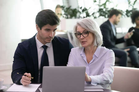 Mature businesswoman use laptop to discuss information with younger colleage. Experienced business...