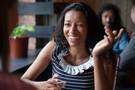 In pub gather diverse people focus on African woman talk with friend, enjoy pleasant conversation in...