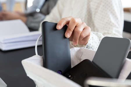 Close up of female employee leaving smartphone engaged in team meeting in office, woman worker place...