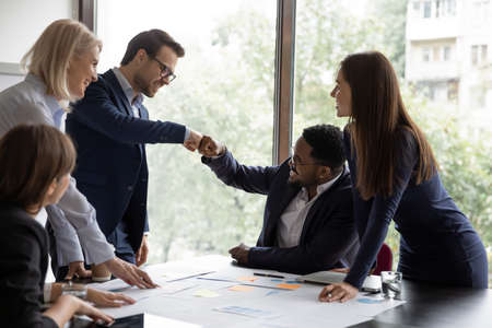 Multi ethnic businessmen project leaders fists bump celebrating corporate achievements, workmates...