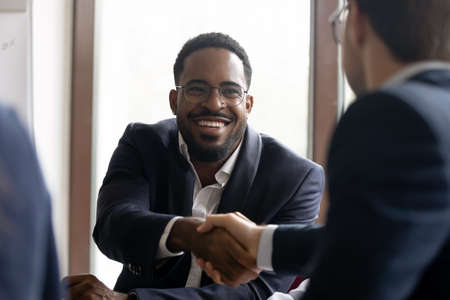 African Caucasian businessmen in formal suits express respect shake hands start negotiations. Common project growth sales increase, partnership, business etiquette, leadership, racial equality conceptの写真素材