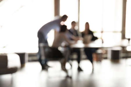 Blurry view of diverse colleagues gather at desk cooperate discuss business ideas together, multiracial employees businesspeople brainstorm work in group team on project in office, teamwork concept