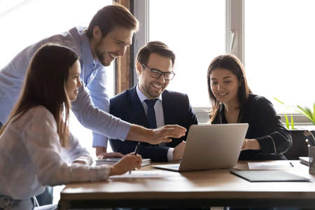Excited multiracial young businesspeople sit in office brainstorm watch funny webinar on computer...