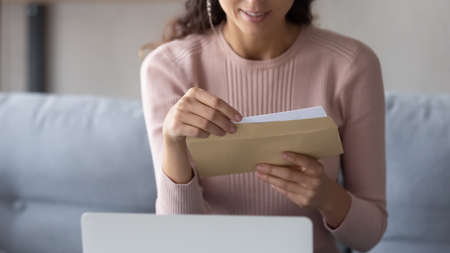 Crop close up of young Caucasian woman hold paper envelope open read postal mail letter at home, female receive post paperwork or document, consider notice or notification correspondence newsの写真素材