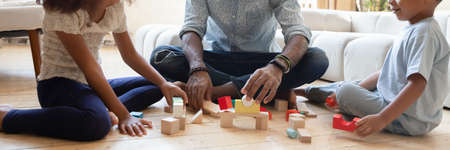 Close up wide banner panorama view of playful african American father with small kids sit on floor...