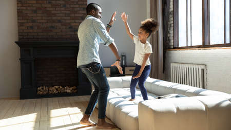 Overjoyed young african american dad have fun with happy little daughter in living room, playful biracial father and small girl child play engaged in funny activity at home, enjoy family weekendの写真素材