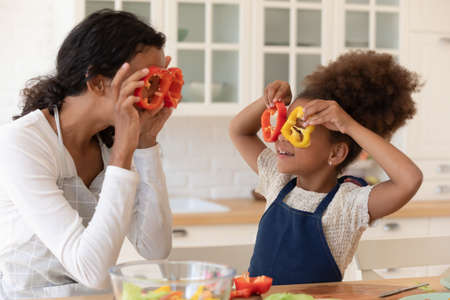 Overjoyed african American young mom and little daughter have fun cooking together in kitchen, happy...