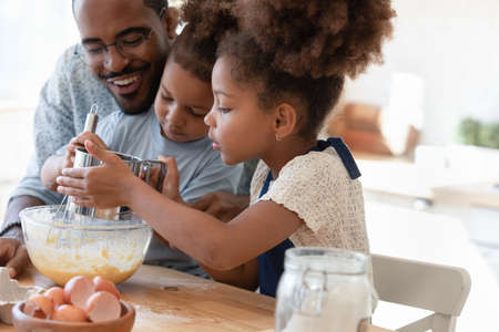 Loving african american father make dough making tasty sweet breakfast pastry with excited little...