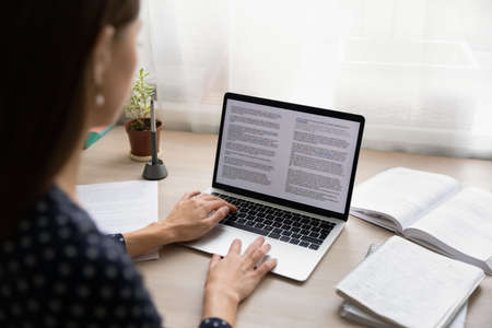 Back view close up of female student sit at desk at home look at laptop screen typing, focused...